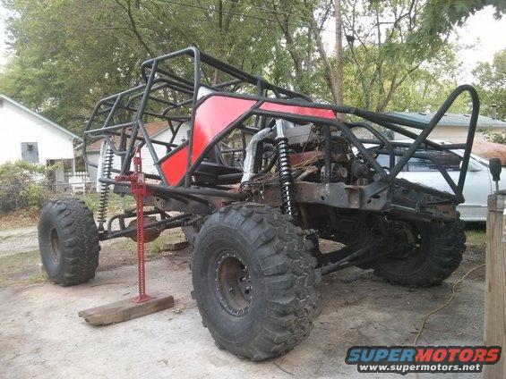 Custom off-road buggy frame with large tires and suspension components, a Hi-Lift jack is positioned under the frame