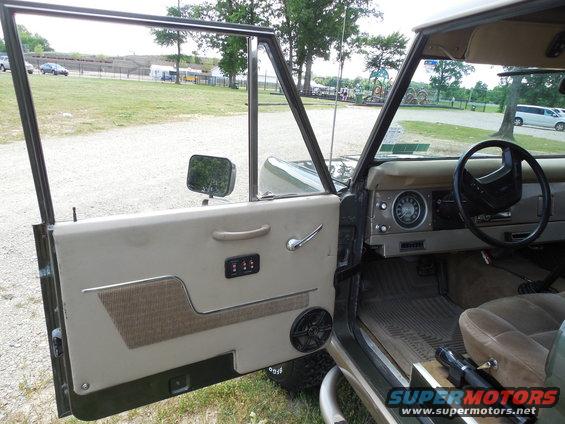 Interior of a 1978 Ford Bronco showing the driver's side door, dashboard, steering wheel, and tan upholstery