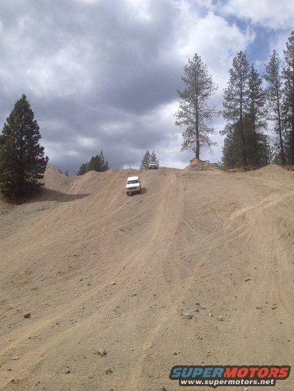 Two white SUVs on a sandy hill under a cloudy sky