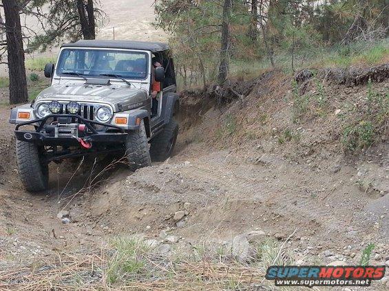 Silver 2005 Jeep Wrangler Rubicon climbing a steep dirt embankment on an off-road trail