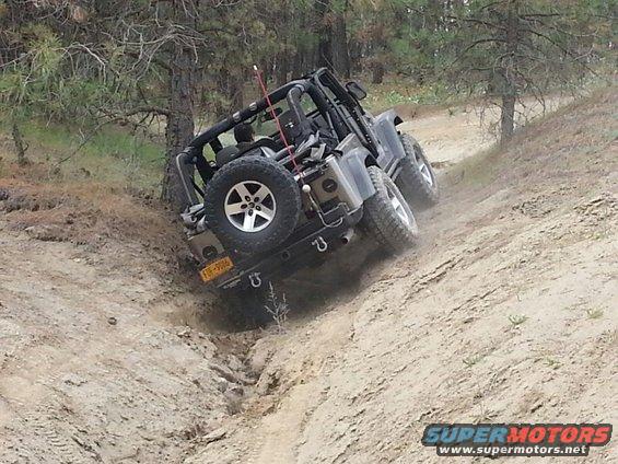 Jeep Wrangler climbing a steep dirt hill with trees around. License plate reads FJF-9006