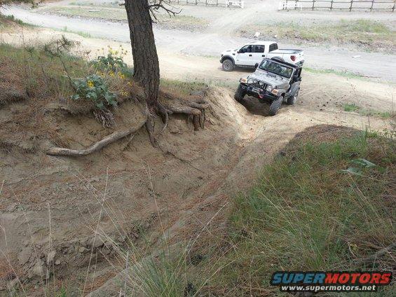 Silver 2005 Jeep Wrangler driving down a dirt embankment with a white pickup truck behind it