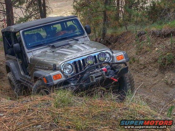 Silver Jeep Wrangler Rubicon with winch on a dirt trail, tires in mud