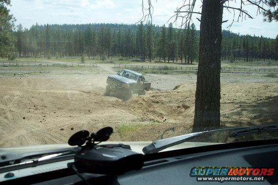 Ford truck driving off-road on a dirt track, kicking up dust. Taken from inside another vehicle