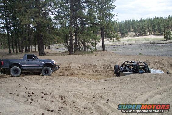 Dark blue pickup truck with off-road tires stuck in sand, another vehicle partially submerged