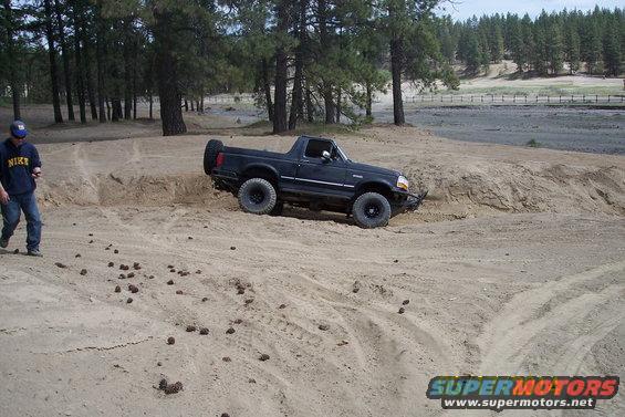 Black 1990 Ford Bronco driving on a sandy hill with a person standing nearby