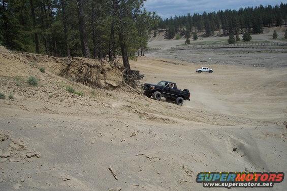 Black 1990 Ford Bronco climbing a dirt hill, white truck in background