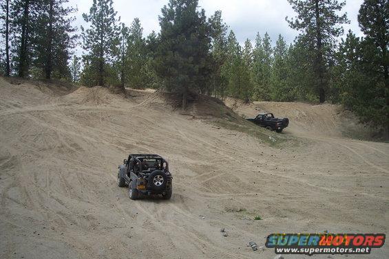 Jeep Wrangler and pickup truck driving on a sandy hill