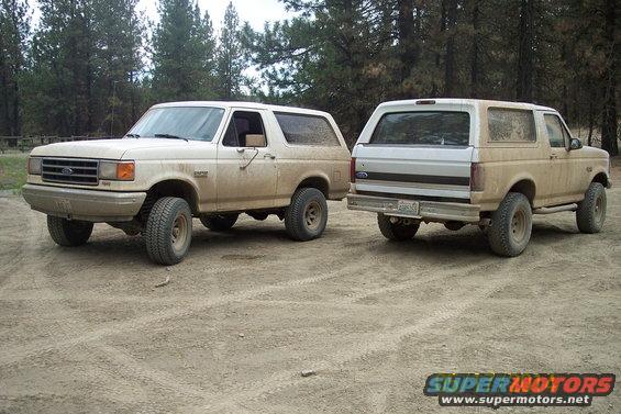 Two tan Ford Broncos parked on a dirt road, one facing front-left, the other facing rear-right