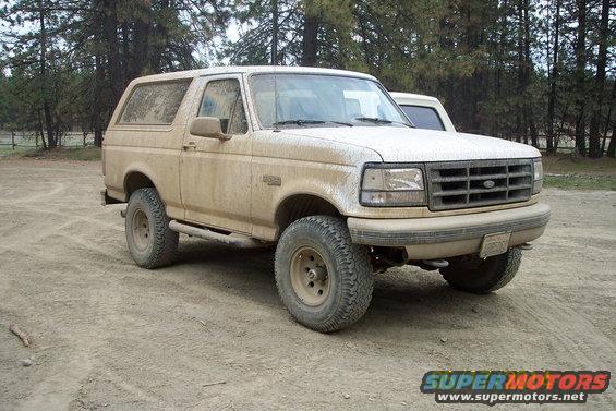 Mud-covered 1990 Ford Bronco parked on a dirt road with trees in the background