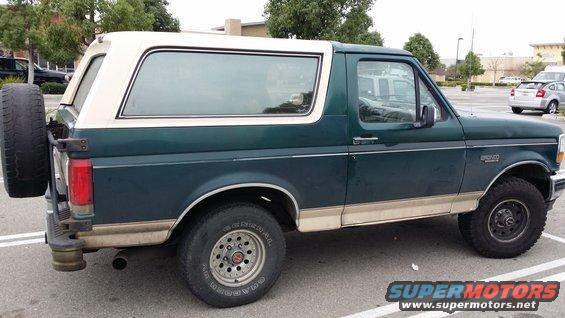 Green and tan Ford Bronco parked in a lot. Spare tire mounted on the back