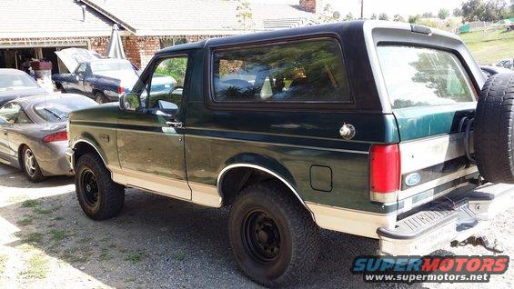 Dark green and tan Ford Bronco with a spare tire mounted on the rear, seen from the rear quarter