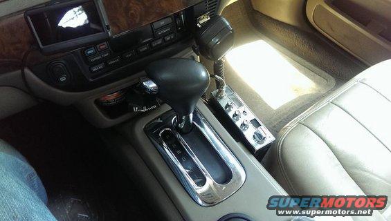 Car's center console with gear shifter, CB radio, and wood trim. Marlboro pack visible