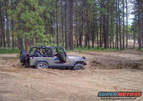2005 Jeep Wrangler stuck in a sandy ditch off-road, trees in background