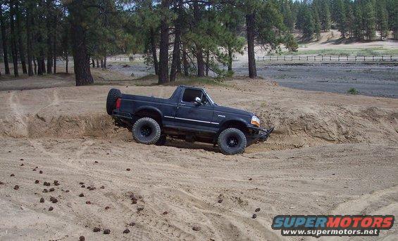 Black Ford Bronco II driving on a sandy trail with trees in the background