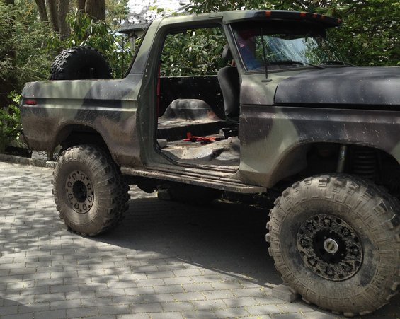 Camouflaged Ford Bronco with doors removed and spare tire mounted on the back
