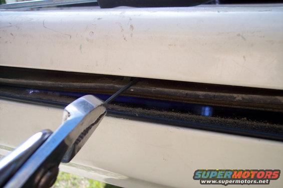 Close-up of a metal rod being inserted into a white tailgate torsion bar mechanism with pliers