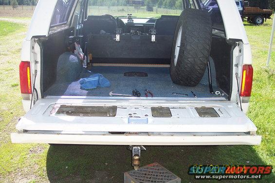 Rear interior of a white 1990 Ford Bronco with tailgate down, spare tire visible