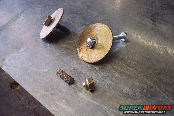 Two screws with large washers and nuts, plus a separate screw and nut, lie on a brushed metal surface