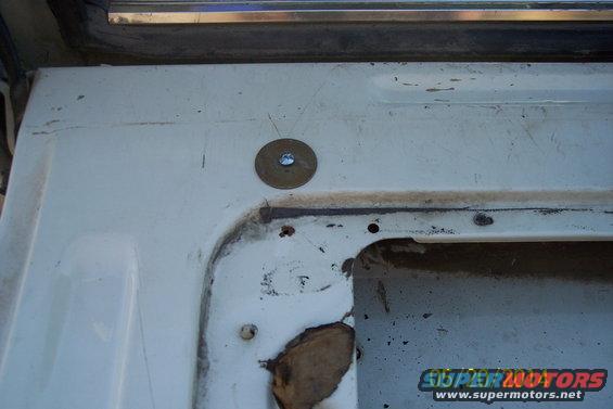 Close-up of a white tailgate interior showing a torsion bar mounting bracket with a washer and bolt