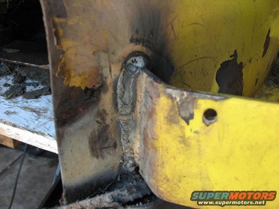 Close-up of a welded metal joint on a yellow frame, showing rust and wear