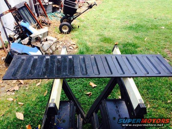 Black tailgate with ribbed texture, resting on sawhorses outdoors