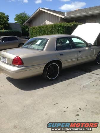 Gold 1998 Ford Crown Victoria with black rims, hood open, parked on concrete