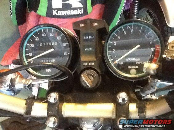 Motorcycle instrument cluster with speedometer, tachometer, and indicator lights. Speedometer reads 27756 mph