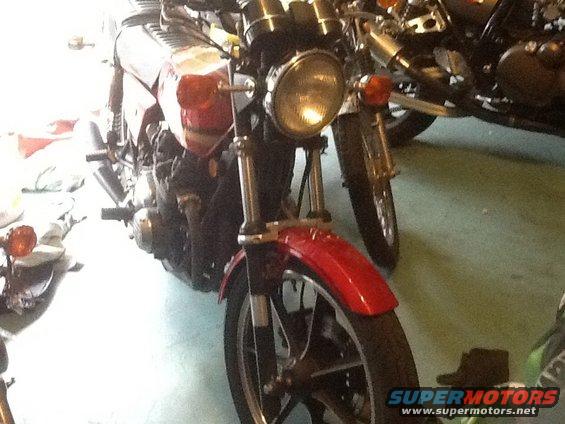 Red motorcycle front fender and headlight assembly, with another motorcycle behind it