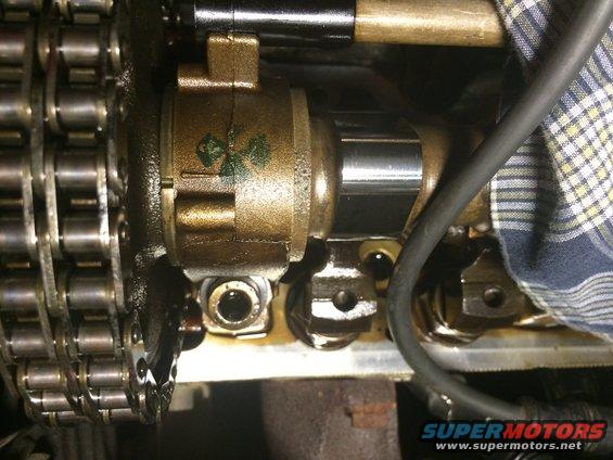 Engine timing chain and brass-colored camshaft components with oil residue. A black hose and checkered cloth are visible