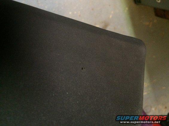 Close-up of a black textured surface with a tiny hole in it. Supermotors.net logo visible
