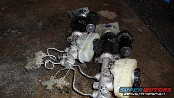 Several brake master cylinders with plastic reservoirs and metal lines on a dark surface