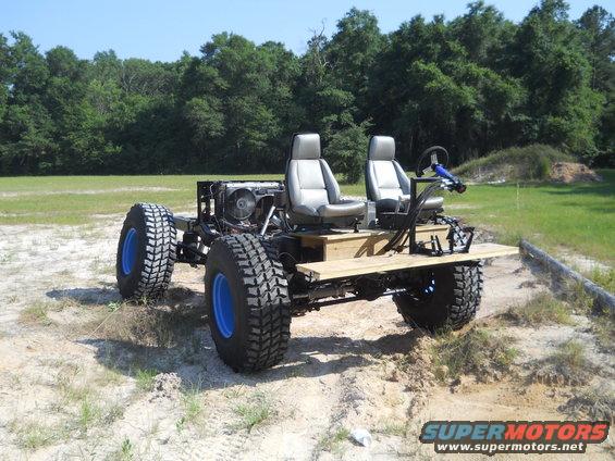 Custom off-road vehicle with two seats, exposed engine, and large tires with blue rims