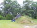 1992 Ford Bronco - An off-road vehicle is tilted on a grassy incline with trees behind it.
