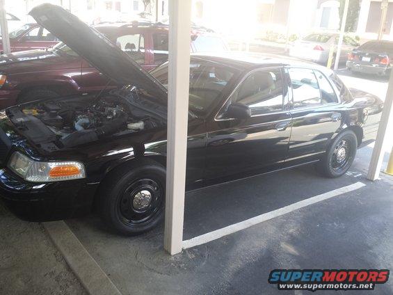 Black 2007 Ford Crown Victoria with hood open, parked in a lot next to another vehicle