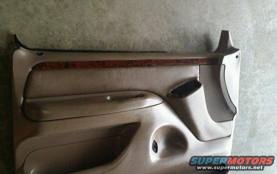 Tan car door panel with wood trim and a torn speaker grille