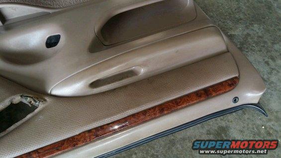 Tan car door panel with wood trim and a torn section near the handle