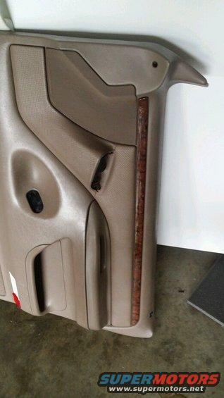 Tan plastic door panel with wood trim and a torn section near the handle