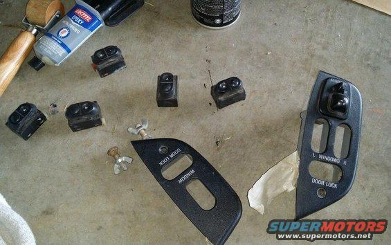 Several car window and lock switches and trim pieces are laid out on a concrete surface next to a tube of Loctite epoxy
