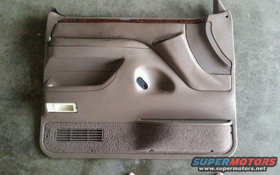 Tan car door panel with wood trim, speaker grille, and storage pocket