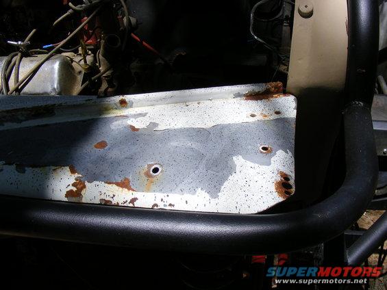 Rusted fender panel with peeling paint and exposed metal, next to black roll bar and engine components