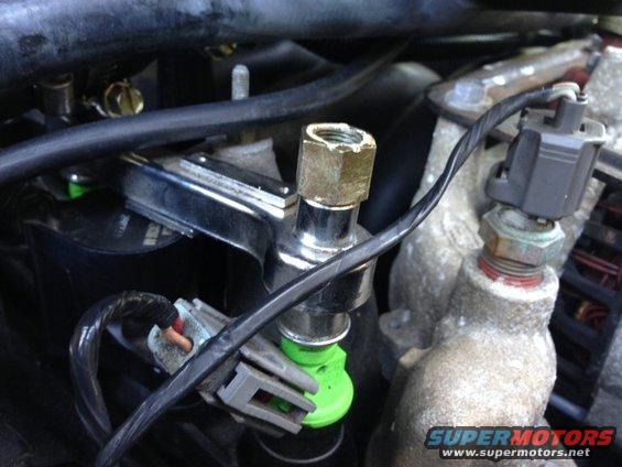Close-up of a fuel injector with a green plastic tip and a sensor screwed into an engine component