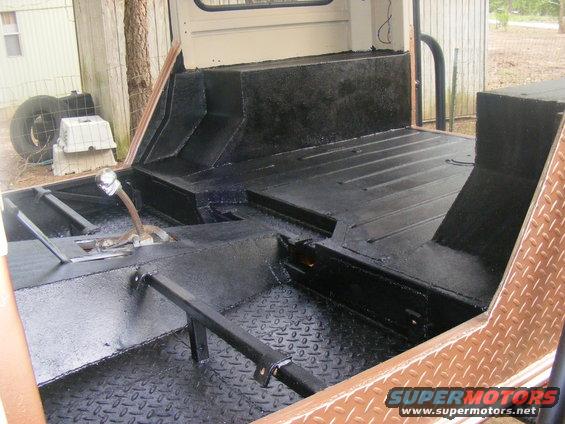 Interior of a vehicle with black diamond plate flooring and black painted surfaces. A shifter is visible