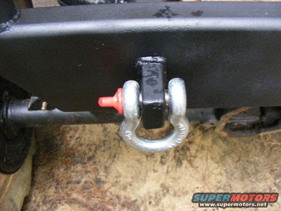 Black tow hitch receiver with a silver shackle attached. Red plastic cap on pin