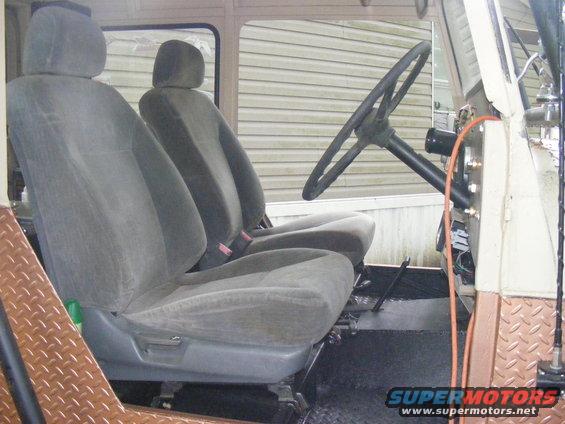 Interior shot of a vehicle with two gray bucket seats, a large steering wheel, and diamond plate trim