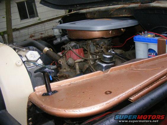 Engine bay with V8 engine, carburetor, and Optima battery. Copper-colored accents on the engine cover and fender