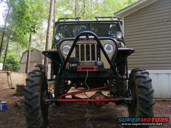 Tan Jeep CJ-5 with large tires and a roll cage, viewed from the front