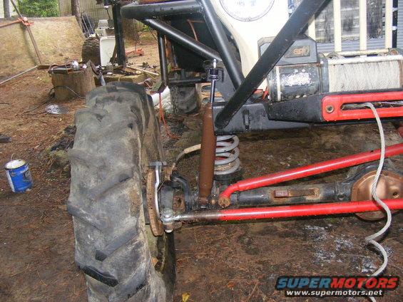 Close-up of a large off-road tire and suspension components, including a shock absorber and red control arms