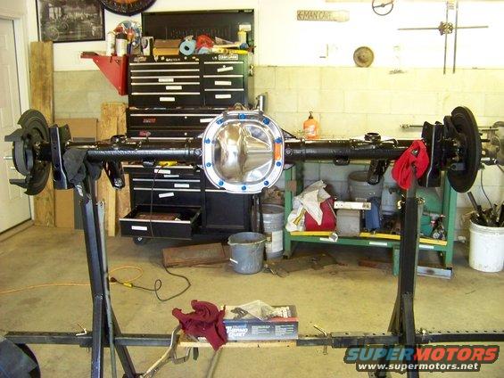 Rear axle assembly on a stand, with brake components attached. A toolbox and shelves are in the background