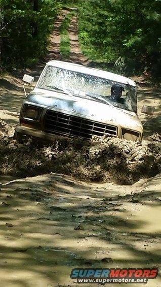 White 1978 Ford Bronco stuck in mud on a dirt track, front 3/4 view